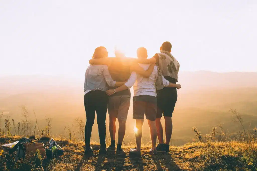 four person hands wrap around shoulders while looking at sunset. Seek support from your friends when experiencing a difficult day.