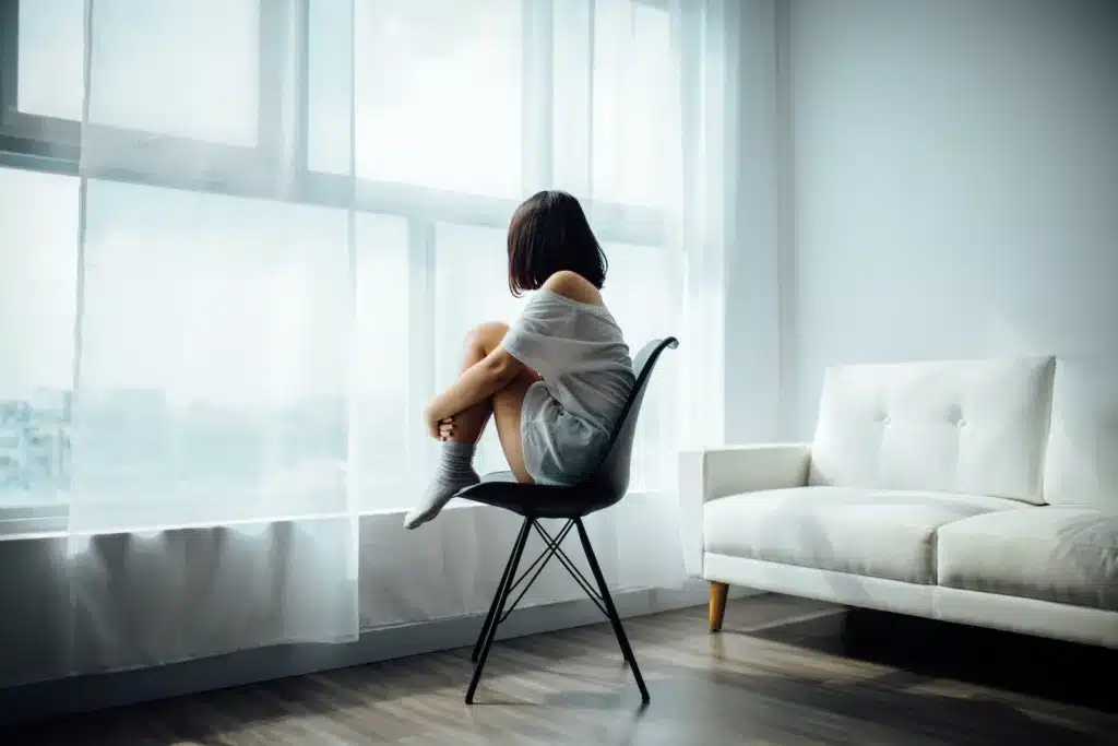 woman sitting on black chair in front of glass-panel window with white curtains. Mindfulness Activities to Reduce Stress & Increase Calm