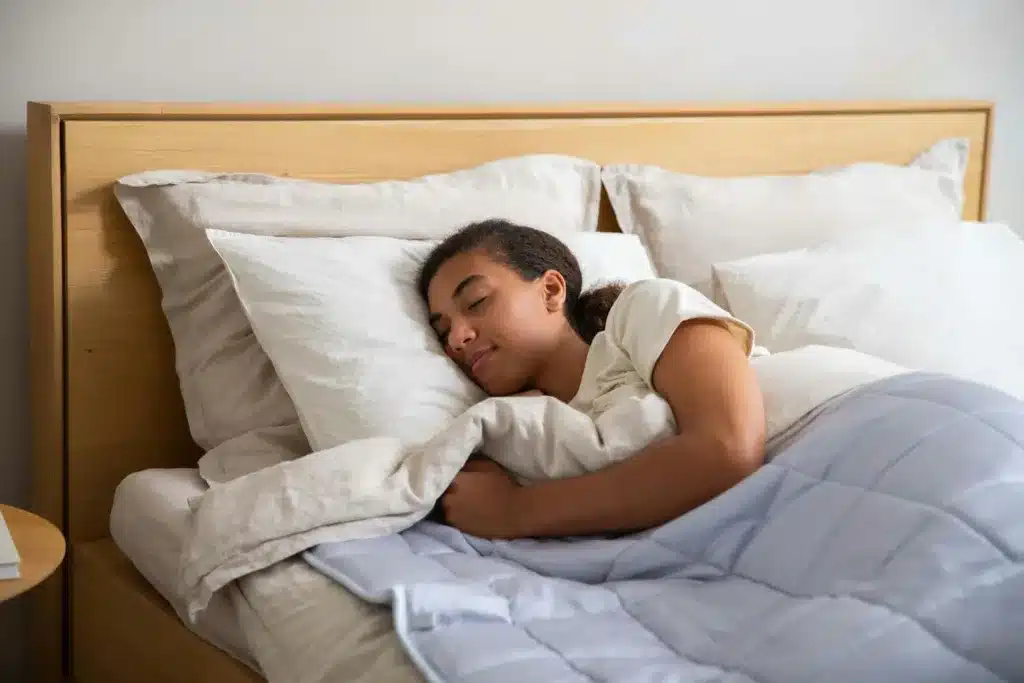 A woman sleeping in a bed with a blanket. natural remedies, sleep wellness, sleep quality, mental well-being 